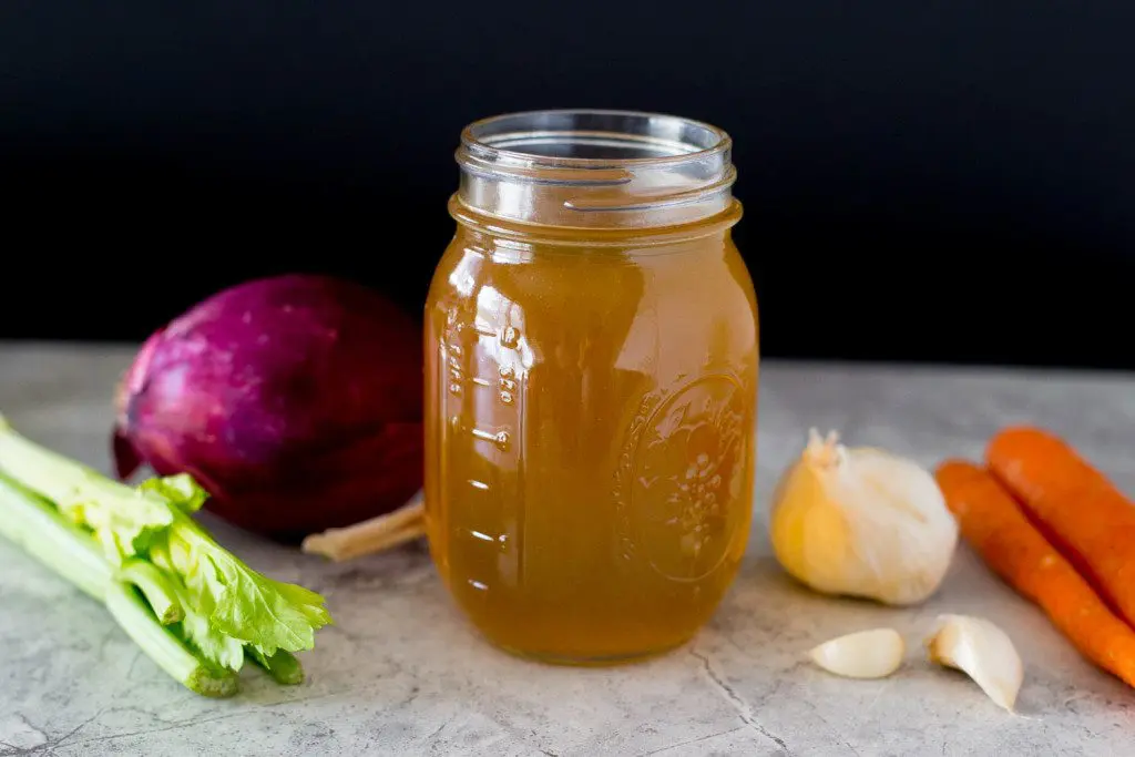 jar of vegetable stock surrounded by fresh vegetables