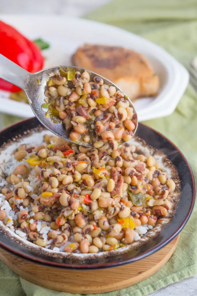 Lowcountry hoppin john made with black eyed peas pouring from a spoon into a big bowl