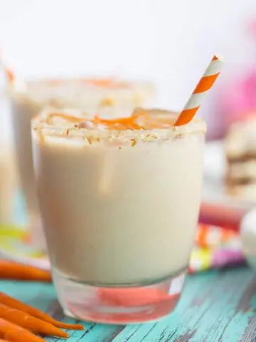 Close up of carrot cake white russian rimmed with cream cheese and garnished with carrot strips and an orange and white striped straw