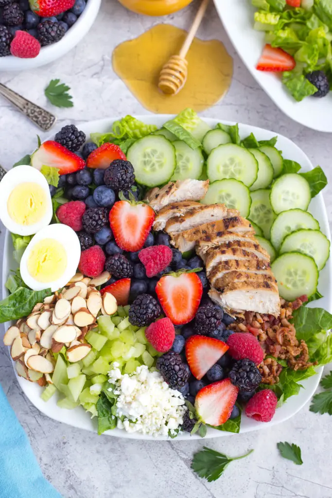 Green Cobb Salad With slivered almonds, a hard boiled egg, mixed berries, grilled chicken, sliced cucumber, and chopped bacon