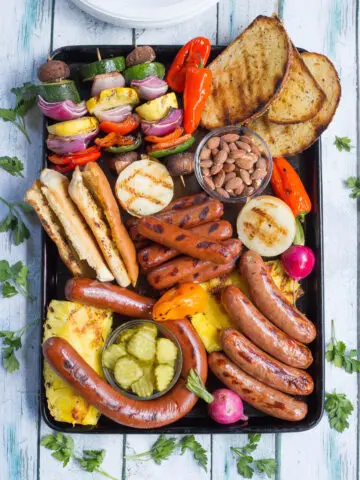 Platter with grilled hot dogs, sausages, pickles, pineapple, peppers, almonds, and bread