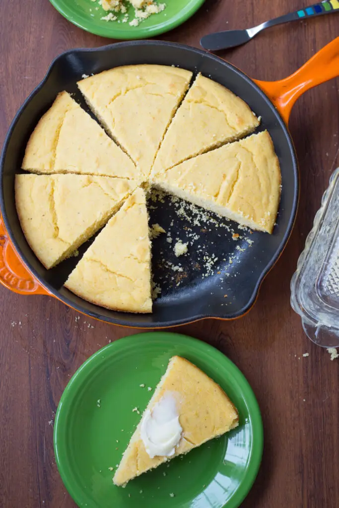 slices of buttermilk cornbread in orange cast iron pan with one slice of cornbread on green plate