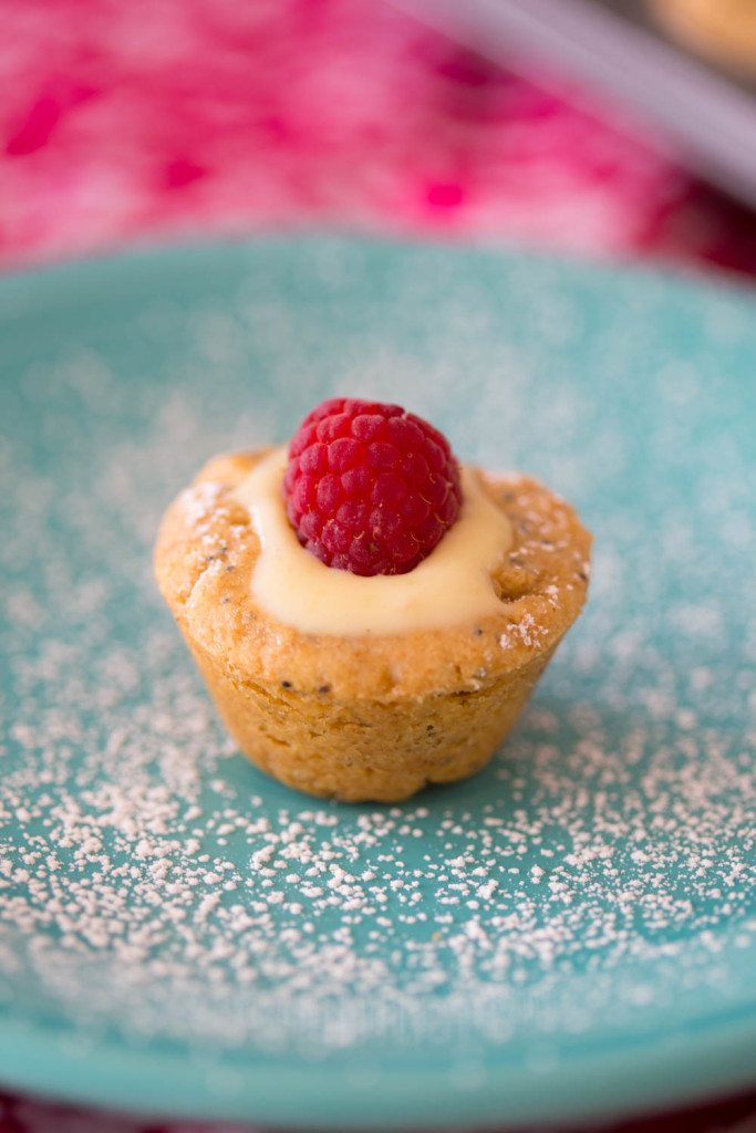 lemon blossom cookie cups shortbread cookies on turquoise plate with powdered sugar topped with a red raspberry