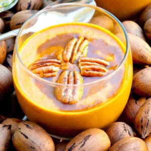 Paleo pumpkin pudding garnished with four pecans and a drizzle of cinnamon syrup in a clear glass