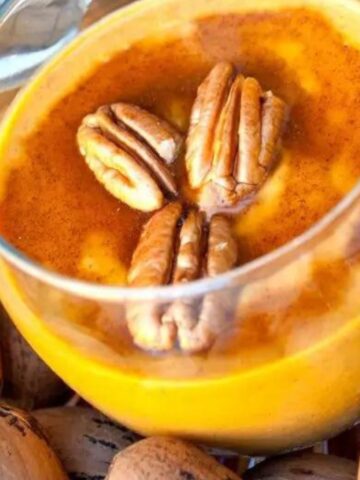 Paleo pumpkin pudding garnished with four pecans and a drizzle of cinnamon syrup in a clear glass