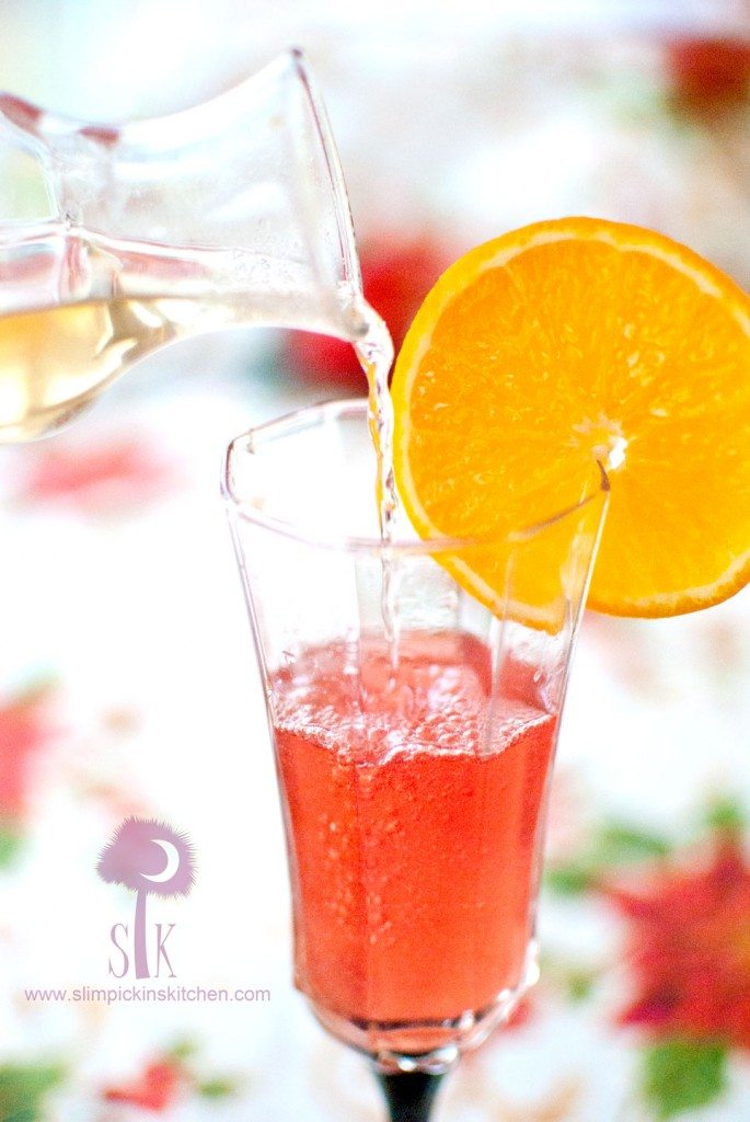 pomegranate poinsetta champagne cocktail being topped off with champagne and garnished with an orange slice