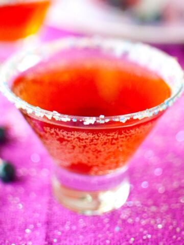 red sugarplum martini in a stemless martini glass on a purple background