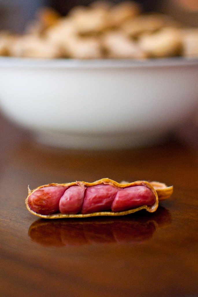 Open red-skinned peanut on brown table with bowl of boiled peanuts in the background