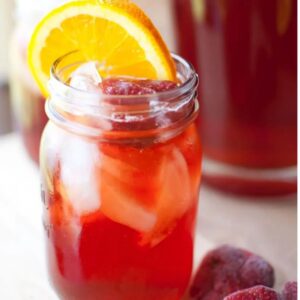 glass of strawberry sweet tea in a mason jar garnished with an orange slice