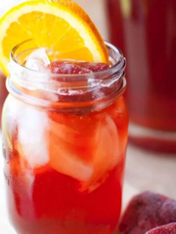 glass of strawberry sweet tea in a mason jar garnished with an orange slice