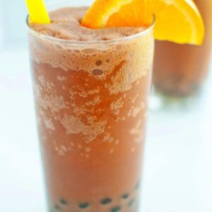 Frozen chocolate orange bubble tea in a glass with black boba and a garnished with a slice of orange
