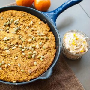 Pumpkin Cornbread speckled with pumpkin seeds in a black cast iron pan w/ a side of gingerbread butter