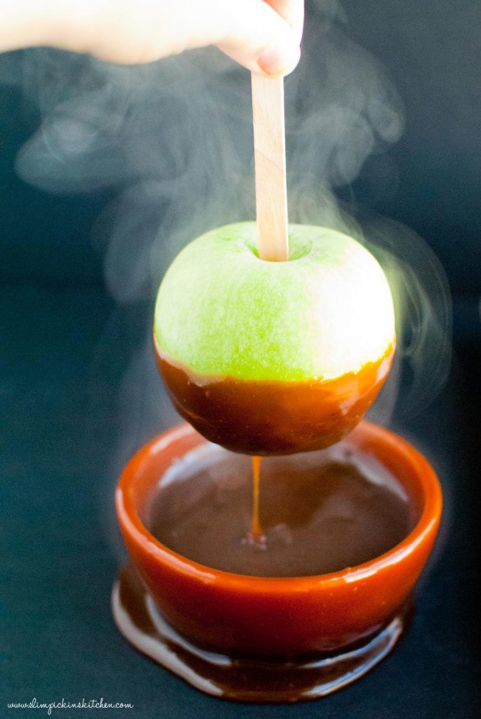 Green apple being dipped in hot caramel with smoking surrounding it