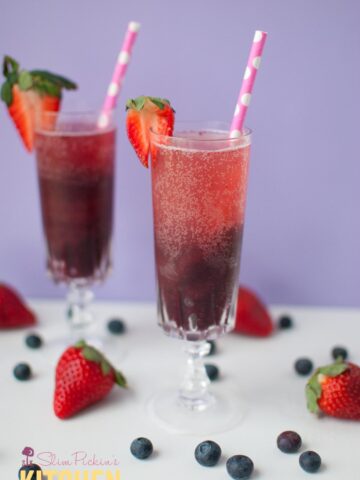 blueberry sorbet in a champagne glass topped with bubbly moscato garnished with a sliced strawberry and a pink straw