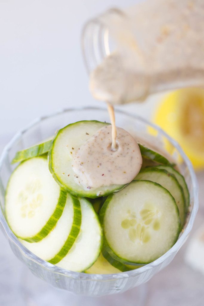 fresh cucumber slices with greek vinaigrette being poured on top