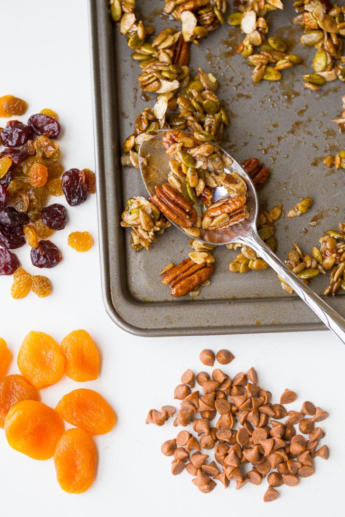 Separated ingredients for maple pumpkin spice trail mix. Cnadied fruit, apricots, and cinnamon chips on the side, with a spoon of trail mix on a cookie sheet. 