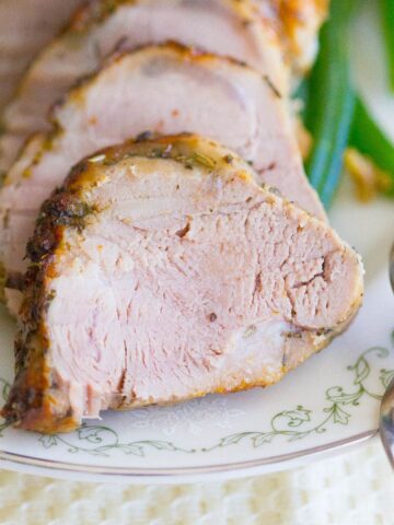 Garlic roasted pork tenderloin cut into rounds displayed on a white plate with green beans beside it.