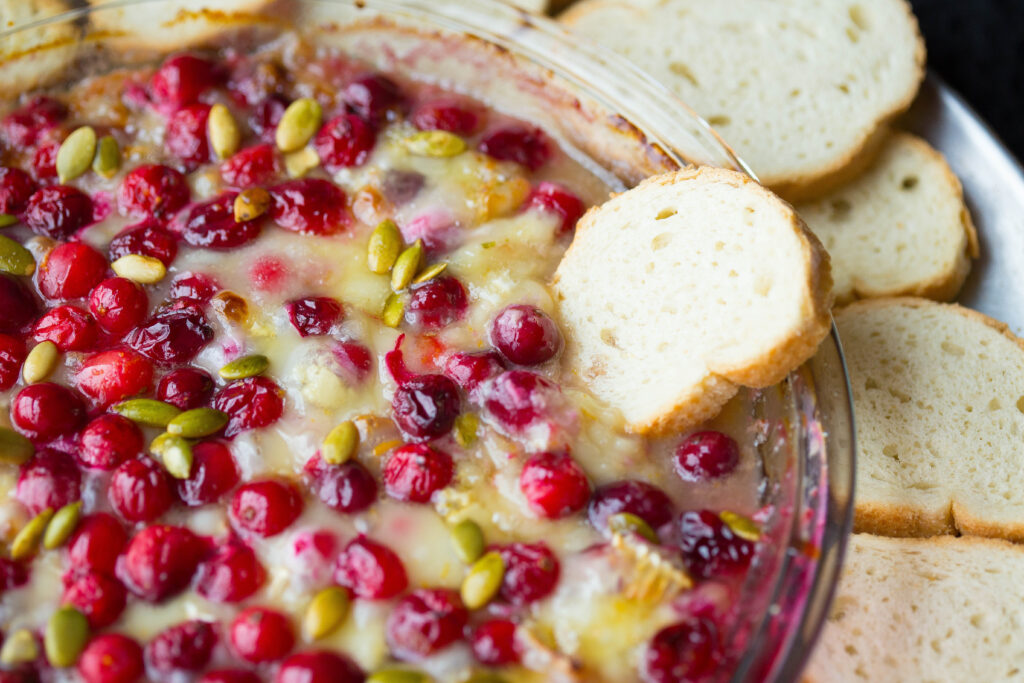 cranberry orange brie dip surrounded by crostini in glass serving dish