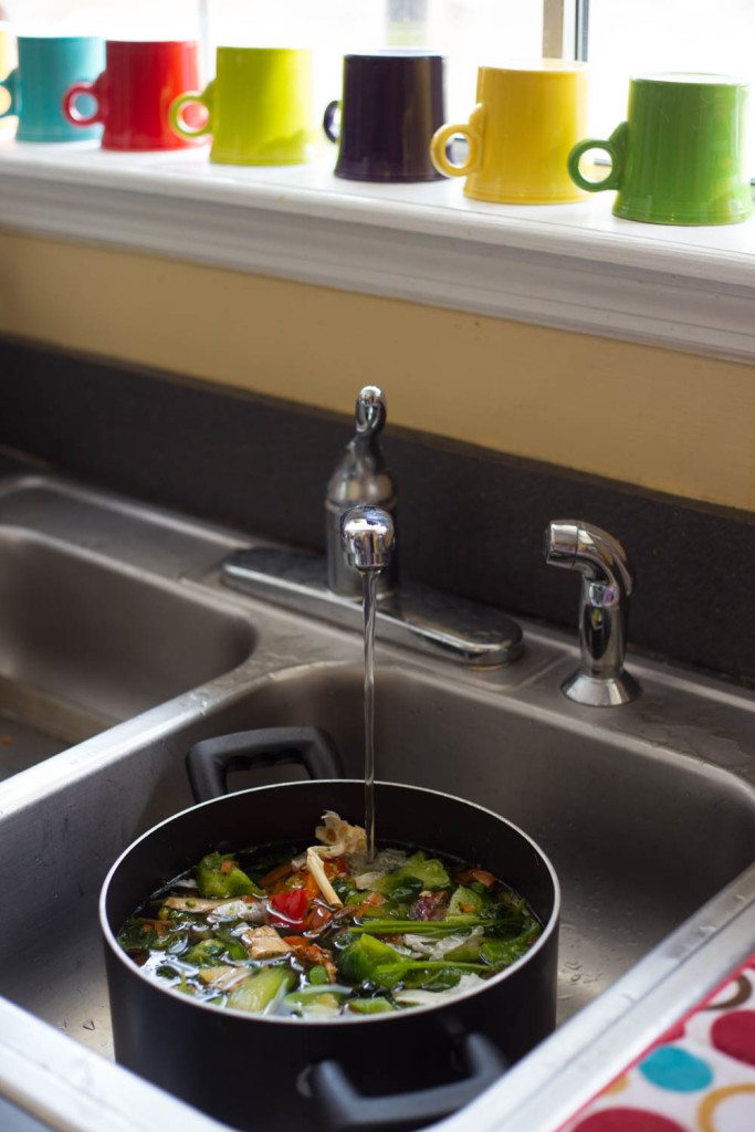 Pot of veggie scraps in the sink with water from faucet pouring on top. 