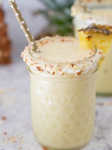 Hummingbird Cake Dairquiri in a small mason jar with cream cheese and coconut garnished with a pineapple