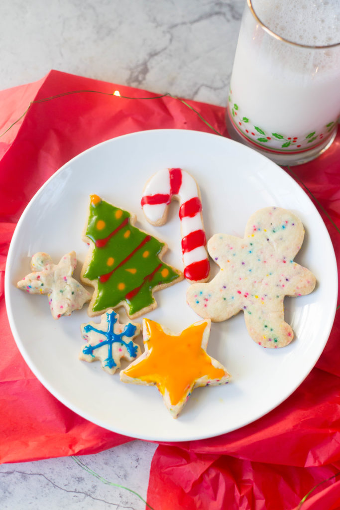 decorated Christmas cookie cut outs on a white plate with a red napkin and a glass of milk