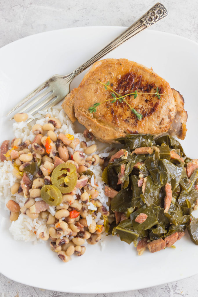 White plate with seared pork chop, instant pot collard greens, ad hoppin john. 