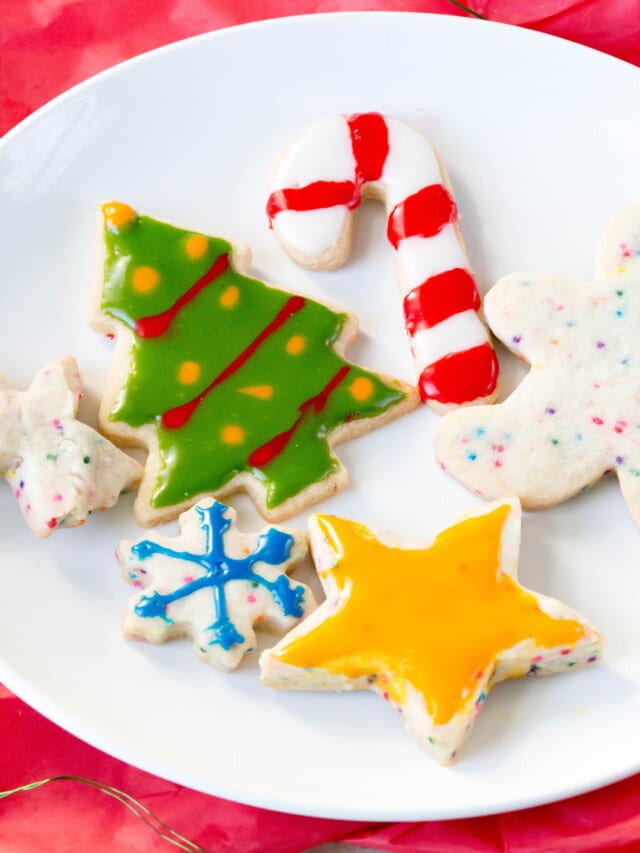 Christmas cut out sugar cookies on a white plate over a red tablecloth