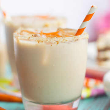 Close up of carrot cake white russian rimmed with cream cheese and garnished with carrot strips and an orange and white striped straw
