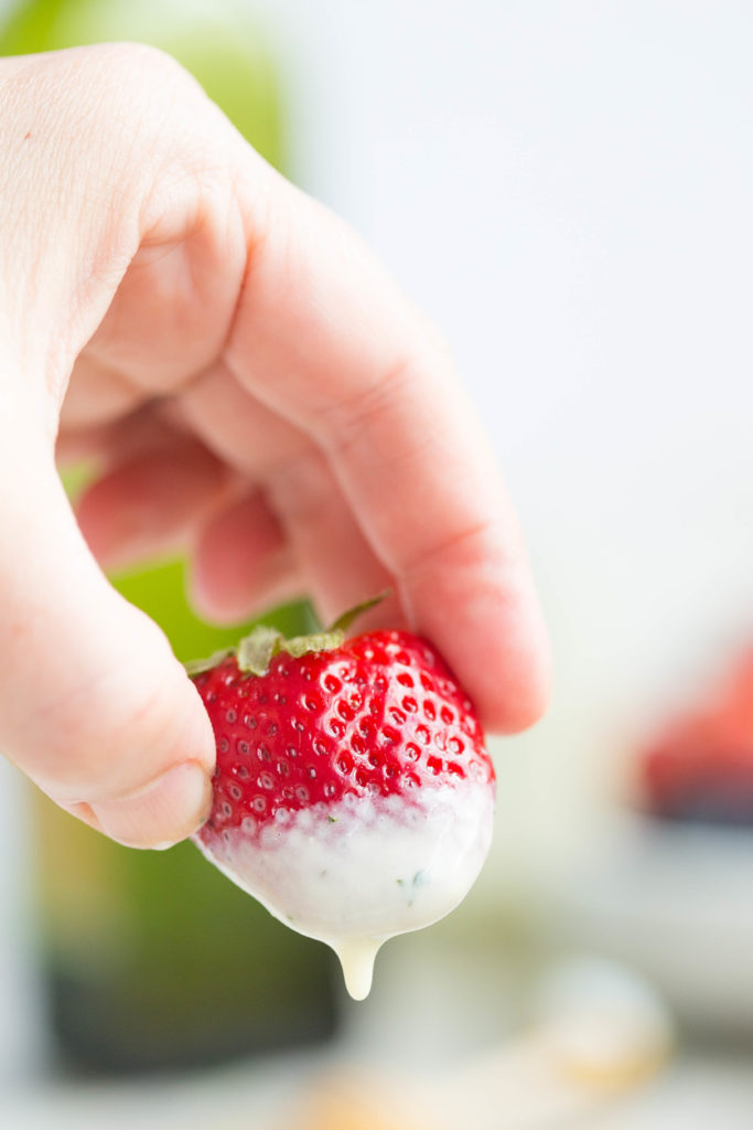 Close up of hand holding a whole strawberry with goat cheese vinaigrette dripping off
