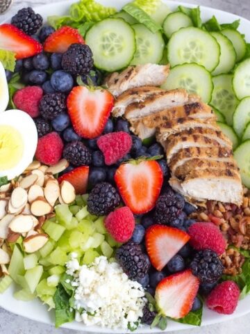 Close up of mixed berry cobb salad with berries, hard boiled egg, grilled chicken, sliced almonds, sliced cucumbers, celery, and bacon
