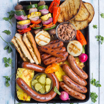 Platter with grilled hot dogs, sausages, pickles, pineapple, peppers, almonds, and bread