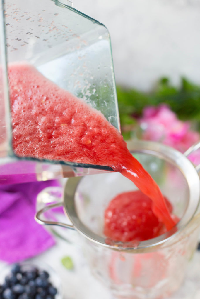 Pink watermelon juice pouring into silver strainer