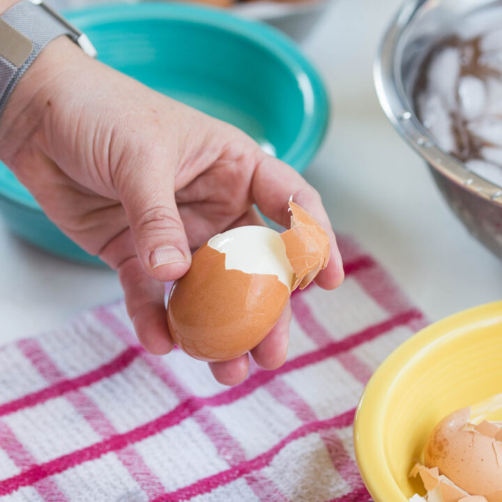 Hand holding an easy peel hard boiled egg with shell halfway off the top