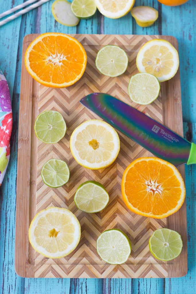 Halved oranges, lemons, and limes on a cutting board with a knife