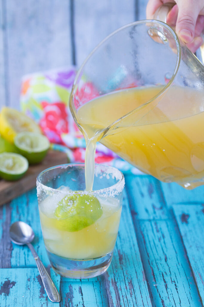 Pitcher of homemade margarita mix pouring into a salt rimmed glass