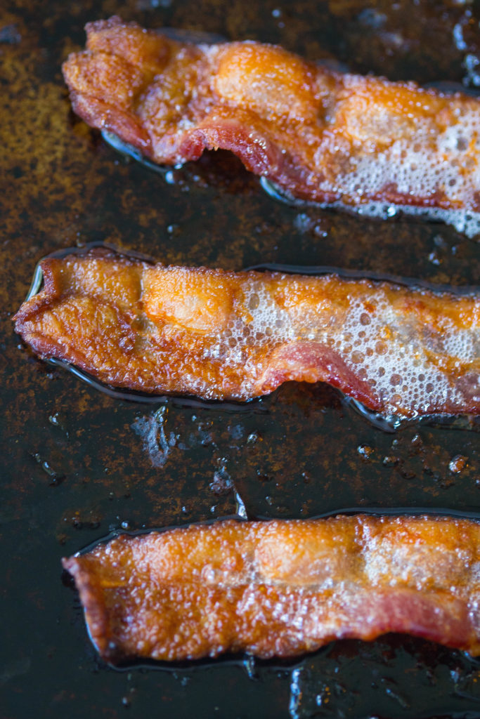 3 pieces of frying bacon on a dark baking sheet