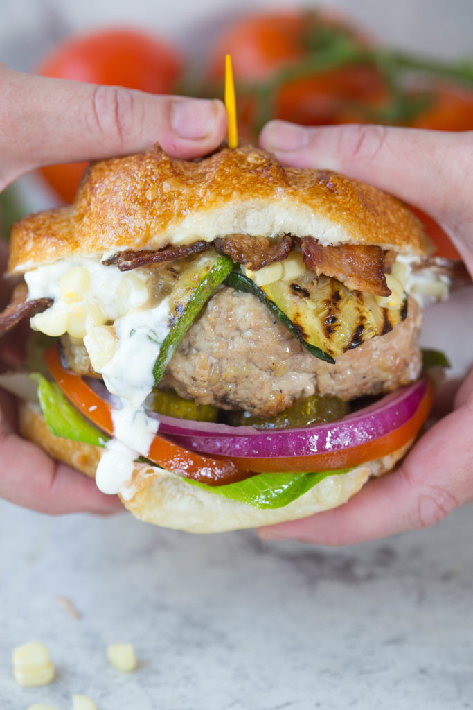 Two hands holding up a turkey burger with dripping basil goat cheese