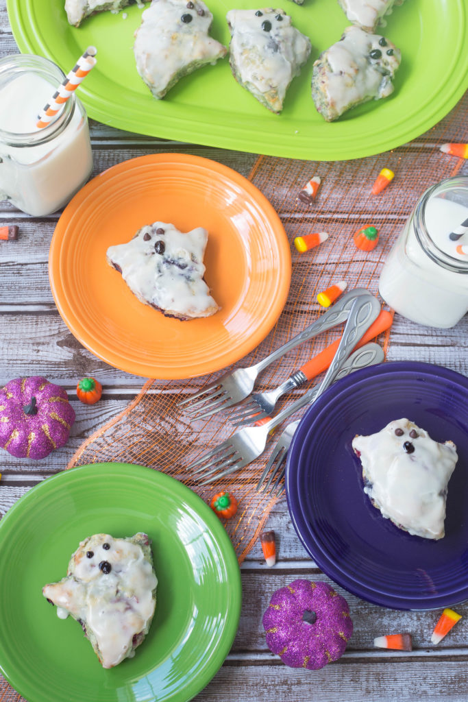 Overhead shot of biscuits decorated like ghosts on lime green, dark purple, and orange fiestaware.