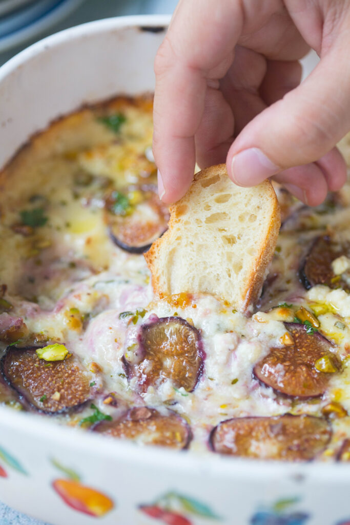 Close up of hand dipping a slice of baguette into baked ricotta