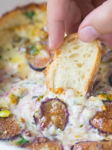 baked ricotta with figs, pistachios, and honey being schooped up with a piece of baguette
