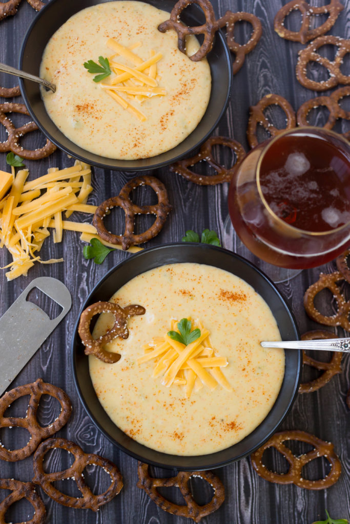 Bowl of Octoberfest Beer Cheese Soup garnished with cheese and parsley and pretzel in black bowl on dark baground