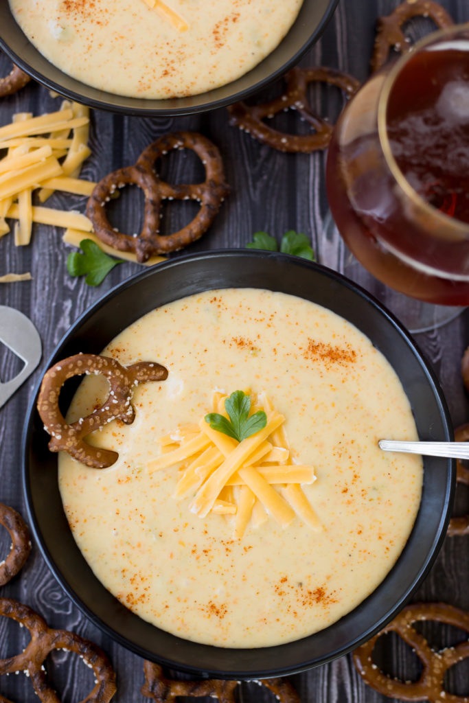 Beer Cheese Soup in black bowl on dark background surrounded by dark pretzels