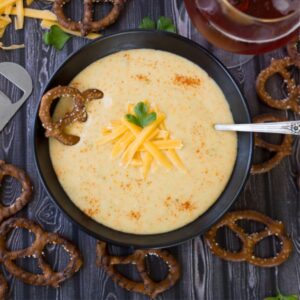 Octoberfest beer cheese soup in a black bowl with a dark brown pretzel garnish