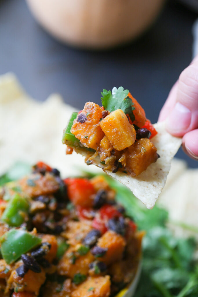 Hand picking up chip with scoop of roasted butternut squash salsa