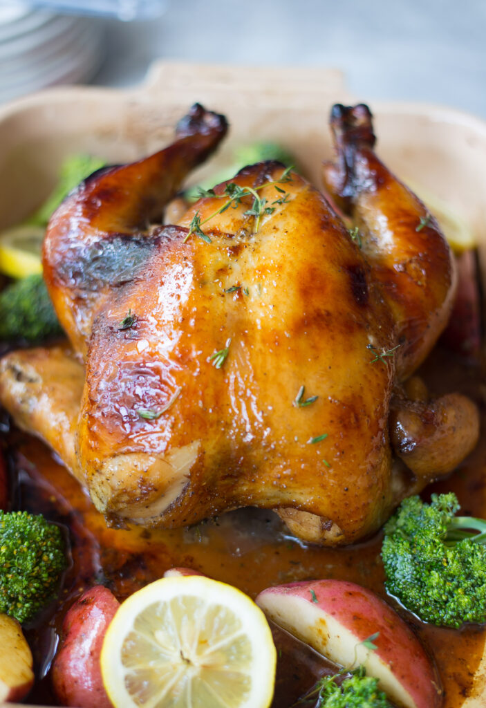 Whole chicken brined in sweet tea on a platter surrounded potatoes, broccoli, and lemons.