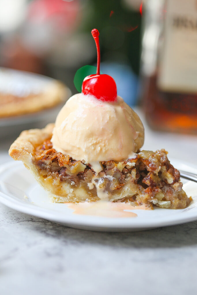 Side view of white chocolate amaretto pecan pie with a scoop of vanilla ice cream with a cherry on top
