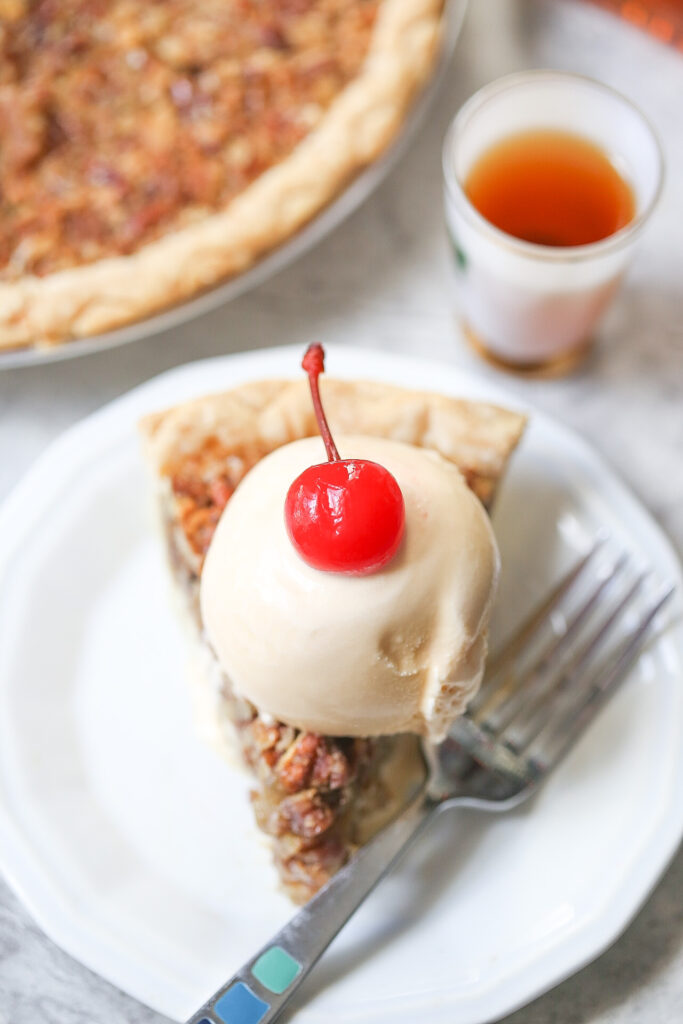 Single slice of white chocolate amaretto pecan pie topped with vanilla ice cream with a cherry