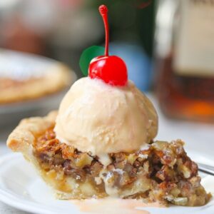 Close up image of white chocolate amaretto pecan pie with melted vanilla ice cream topped with a red cherry
