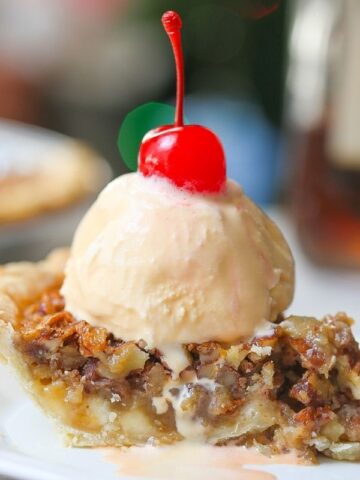 Close up image of white chocolate amaretto pecan pie with melted vanilla ice cream topped with a red cherry