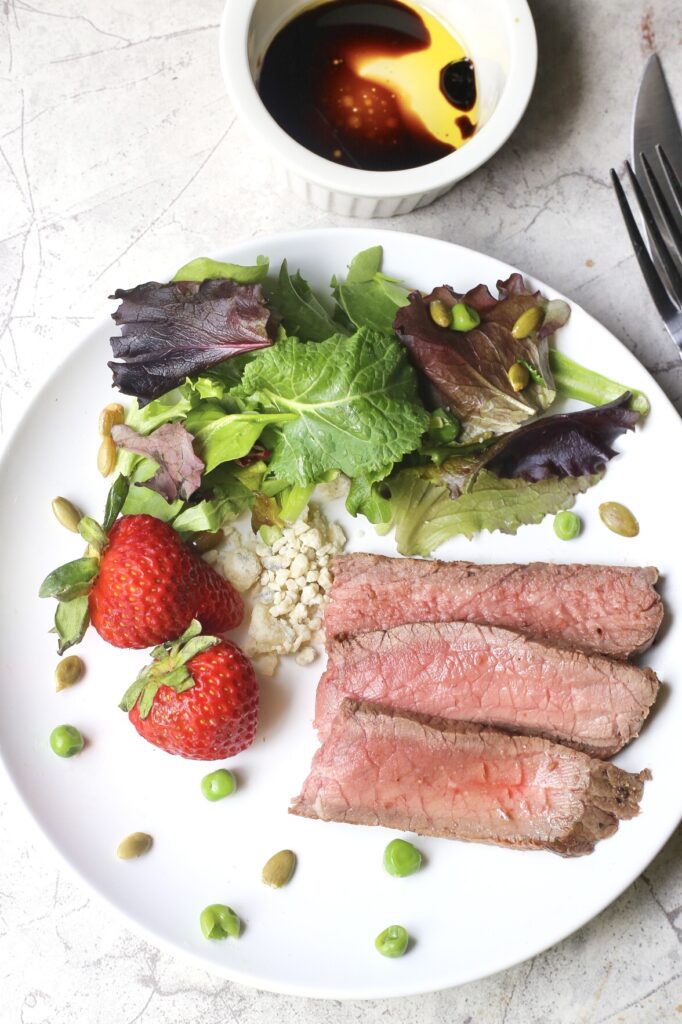 Easy London Broil on white plate with salad and peas
